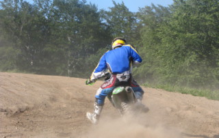 Pohled ze zadu na motorku s Milanem v prašné zatáčce